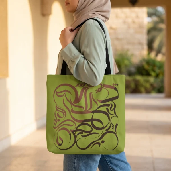 Product photoshoot of abstract Arabic calligraphy Kunafa Chocolate tone tote bag held by a model - tote size 16"X16" - binmahmood