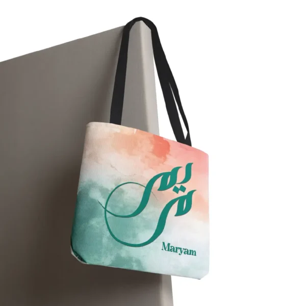 Maryam name in BinMahmood original Arabic fusion calligraphy in teal ink on a polyester tote bag with black handles, soft coral and mint watercolour background, white product view — mouse-crafted by BinMahmood