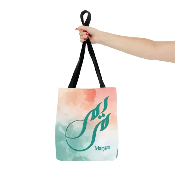 Maryam name in BinMahmood original Arabic fusion calligraphy in teal ink on a polyester tote bag with black handles, soft coral and mint watercolour background, white product view — mouse-crafted by BinMahmood