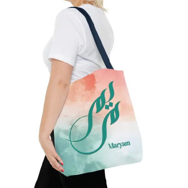 Maryam name in BinMahmood original Arabic fusion calligraphy in teal ink on a polyester tote bag with navy handles, soft coral and mint watercolour background, white product view — mouse-crafted by BinMahmood