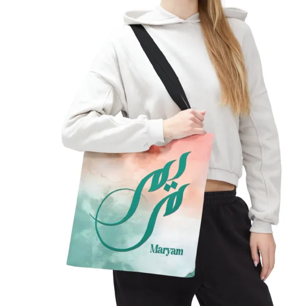 Maryam name in BinMahmood original Arabic fusion calligraphy in teal ink on a polyester tote bag with black handles, soft coral and mint watercolour background, white product view — mouse-crafted by BinMahmood