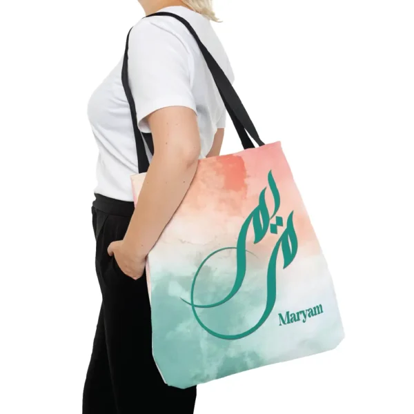 Maryam name in BinMahmood original Arabic fusion calligraphy in teal ink on a polyester tote bag with navy handles, soft coral and mint watercolour background, white product view — mouse-crafted by BinMahmood