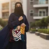A beautiful lifestyle composition showing the Zeenat personalized calligraphy tote bag carried by a woman carried by a modest woman wearing abaya, hijab and niqab