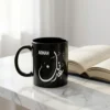 Product photography of Adnan customized Arabic Diwani calligraphy name black mug place on a marble top with a book open in the background - binmahmood