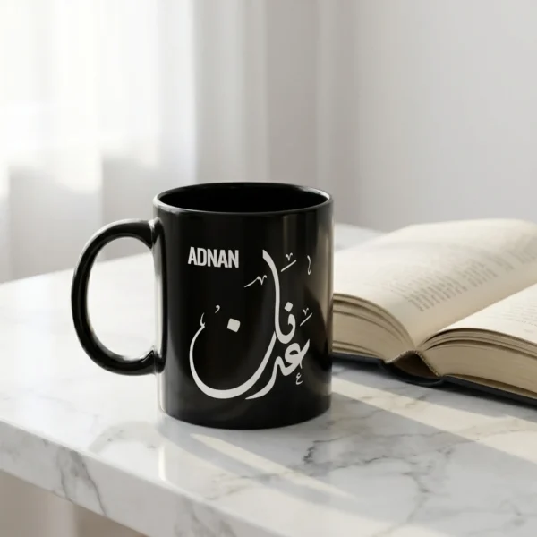 Product photography of Adnan customized Arabic Diwani calligraphy name black mug place on a marble top with a book open in the background - binmahmood