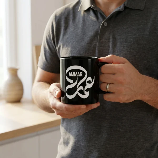 Product photoshoot of Ammar Arabic calligraphy black mug by binmahmood held in hands by a male model wearing a polo shirt