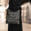 Product photoshoot of Arabic Viral Meme Tote Bag crafted in Diwani Calligraphy - the model is holding the bag shoulder down on a busy metro station - binmahmood