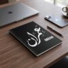 Product photoshoot of Imran Arabic Diwani calligraphy name art spiral notebook, lay flat on a dark wood table, a closed apple laptop and an i phone along with a pen can be seen in the blur background - binmahmood