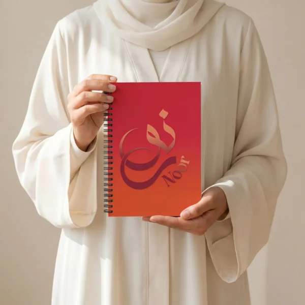 Product photoshoot of Noor Arabic calligraphy notebook, held a woman wearing a modest off white Abaya - binmahmood