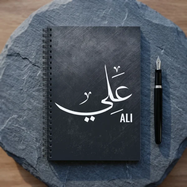 Product photoshoot of Ali personalized Arabic name Thuluth calligraphy spial notebook place on a slate colour hard surface with a pen - binmahmood