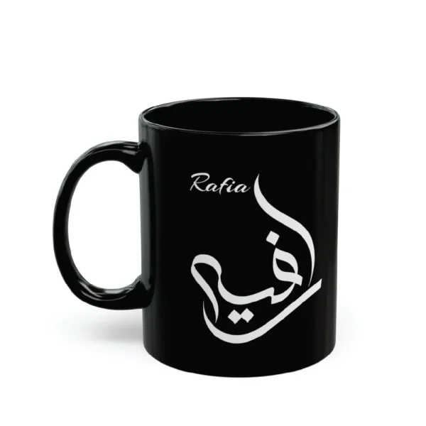 A model in a cream-colored outfit holding a glossy black ceramic mug featuring the name Rafia in white Al Wissam Arabic calligraphy. The design is precision mouse-crafted and displayed in a minimalist lifestyle setting.