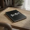 Product photography of Saeed Arabic Al Wissam calligraphy name art spiral notebook, lay flat on cane table - binmahmood