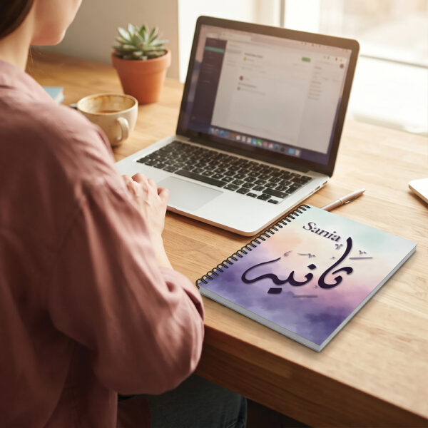 Product photography of Sania Arabic Diwani calligraphy name art spiral notebook, lay flat on an office table - binmahmood