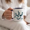 Model photoshoot of Sofia Arabic Calligraphy Mug in Diwani Script with a dark blue handle and inner, held by a model in her hands, the mug sits on the knees of the model